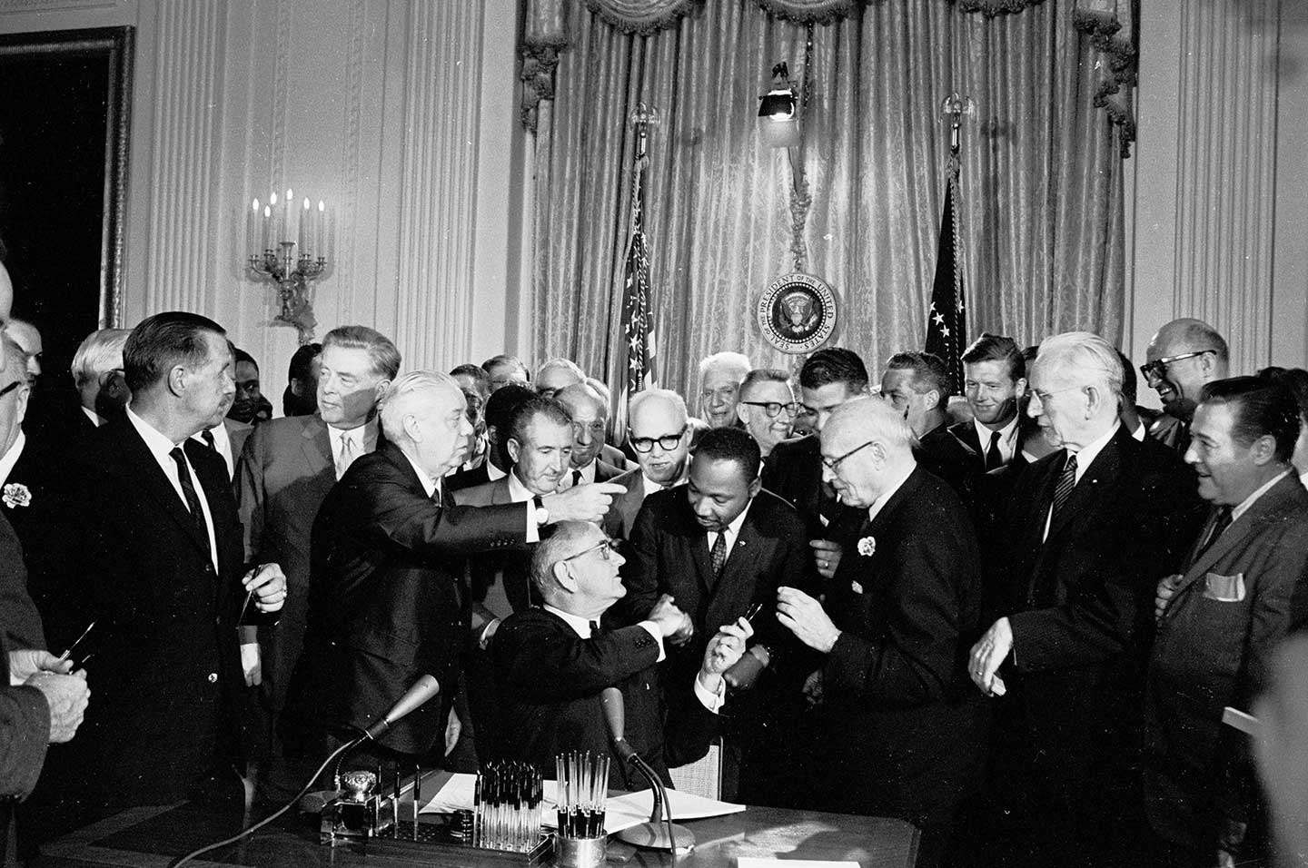 President Lyndon B. Johnson signs the 1964 Civil Rights Act as Martin Luther King, Jr., and others look on.