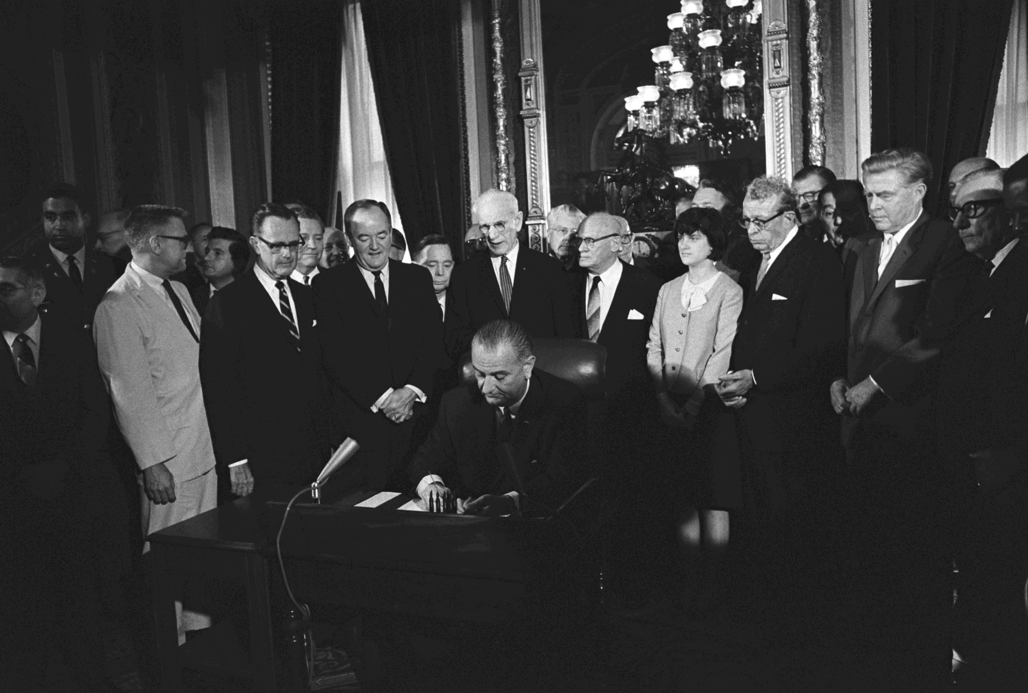 President Lyndon B. Johnson seated at bill signing table as others look on from behind him.
