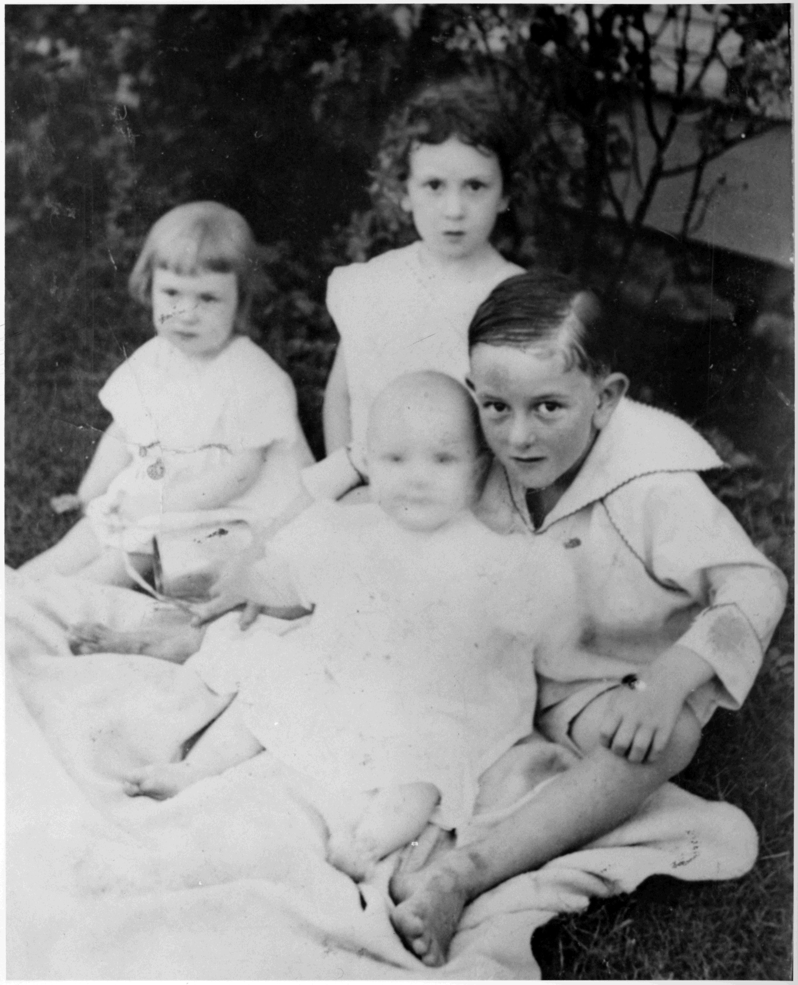 LBJ poses with his three siblings while all seated on a blanket in a yard.