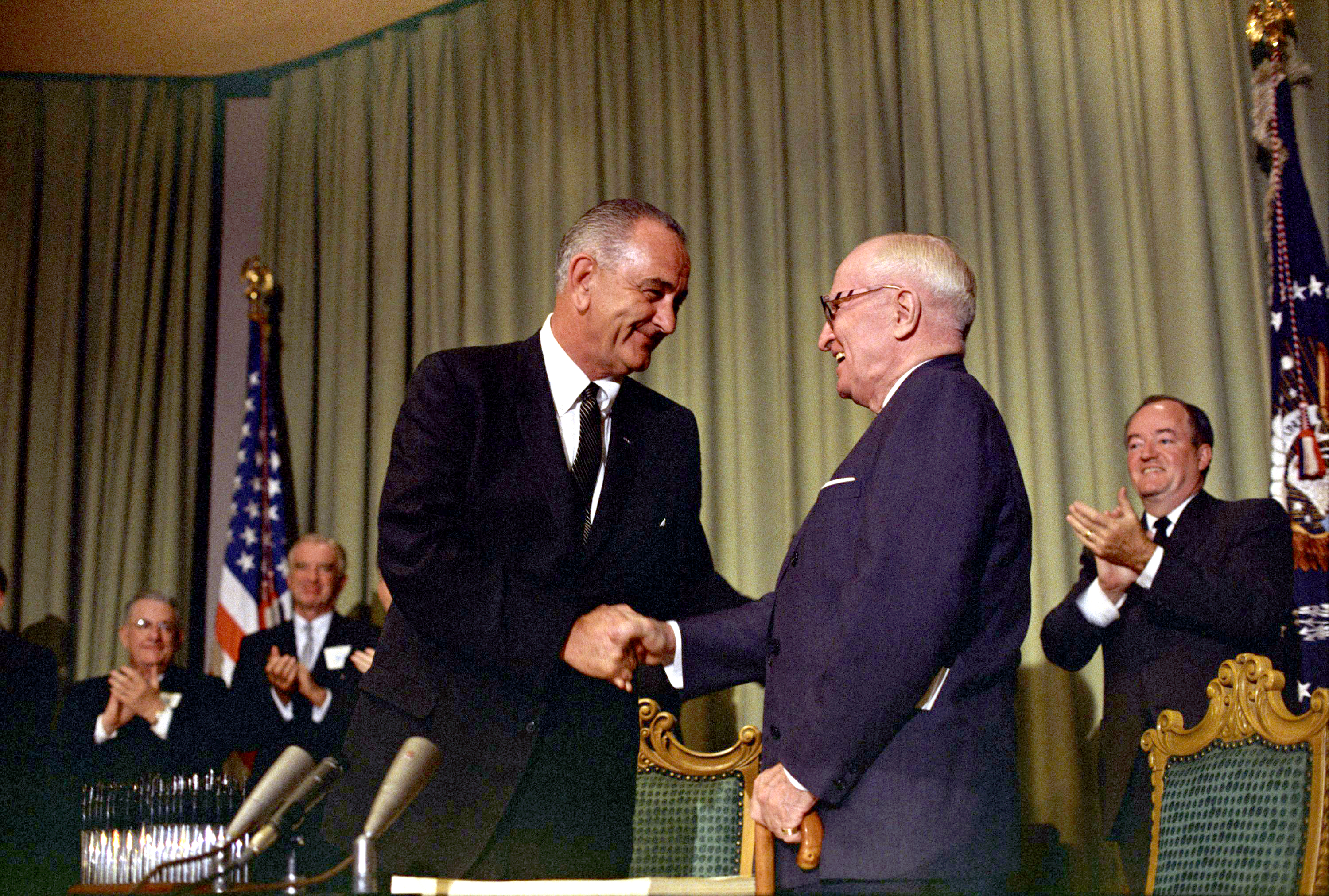 President Lyndon B. Johnson shakes hands with President Harry S. Truman as others (in background) applaud. LBJ Library photo by Unknown #34897-14.