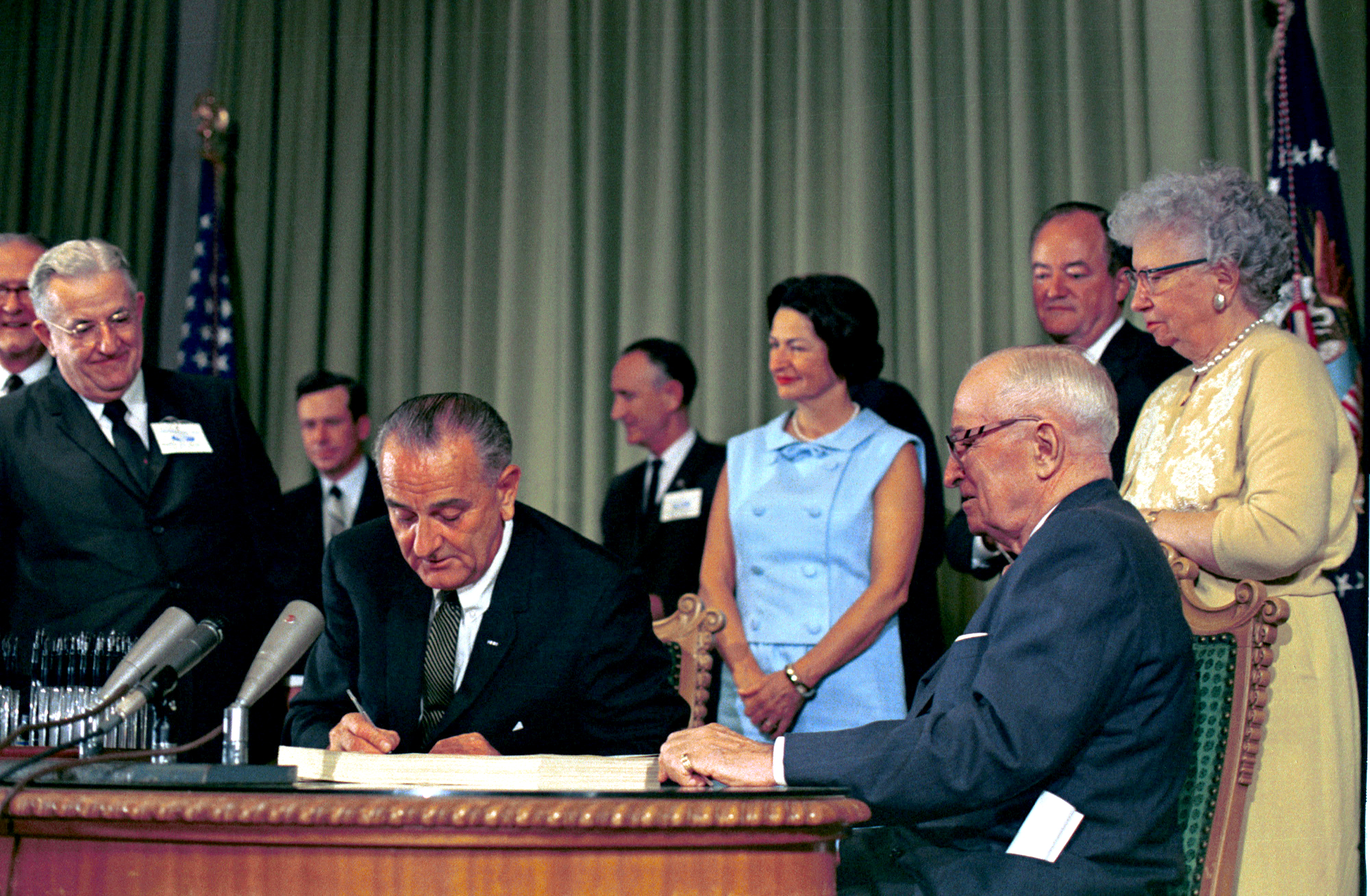 President Lyndon B. Johnson hands a signing pen to Bess Truman as President Harry S. Truman, Lady Bird Johnson and others look on.  LBJ Library photo by unknown #34897-16.