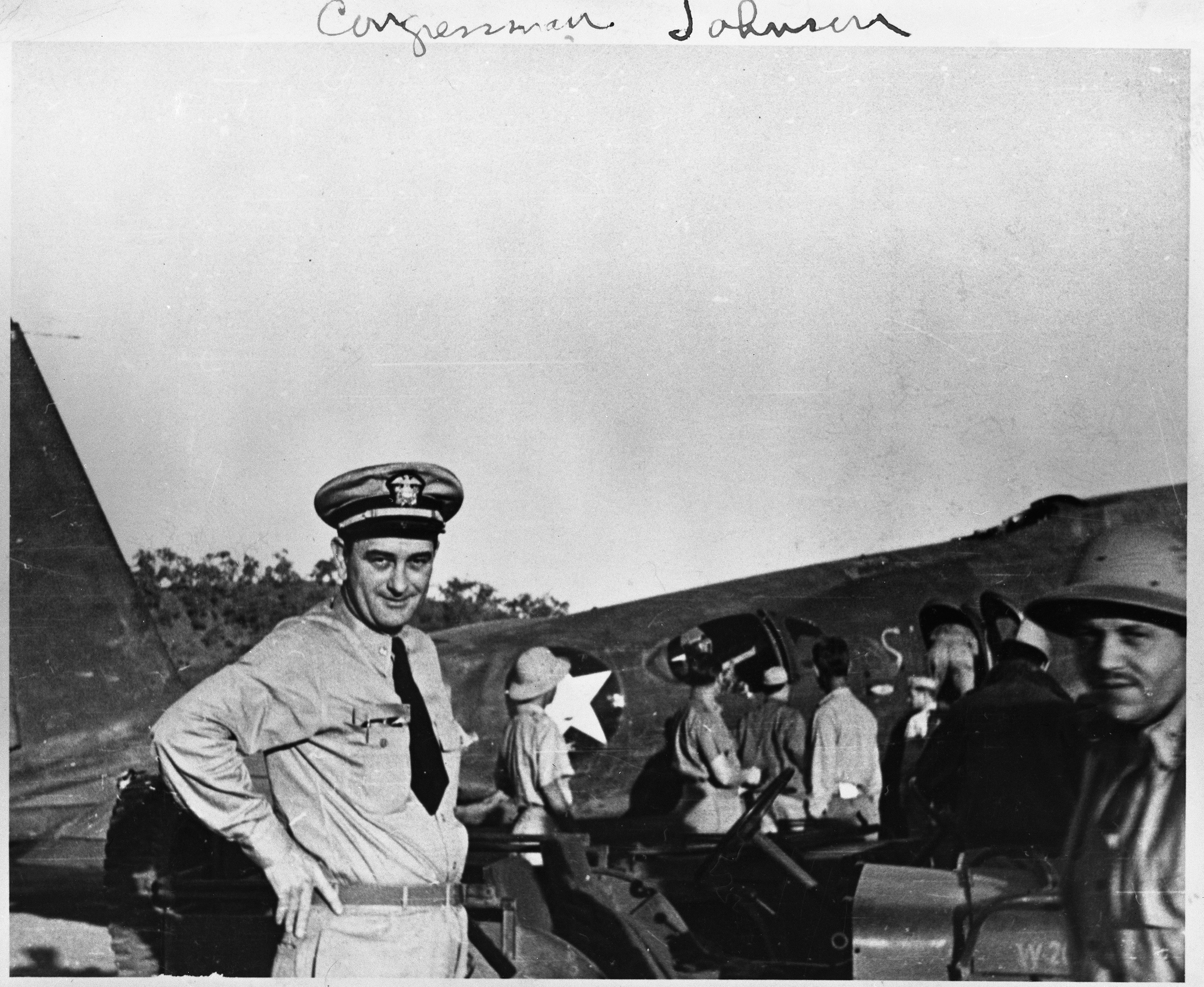 Lt. Commander Lyndon. B Johnson, dressed in his Naval uniform, poses in front of an aircraft at the Seven Mile Air Drome, New Guinea.