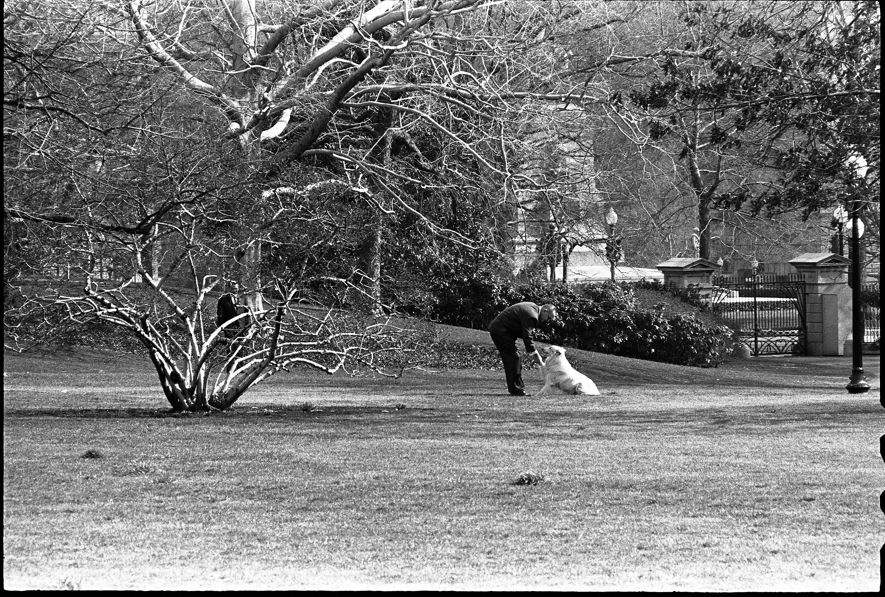 President Johnson holds his dog, Blanco, paw while leaning over him.