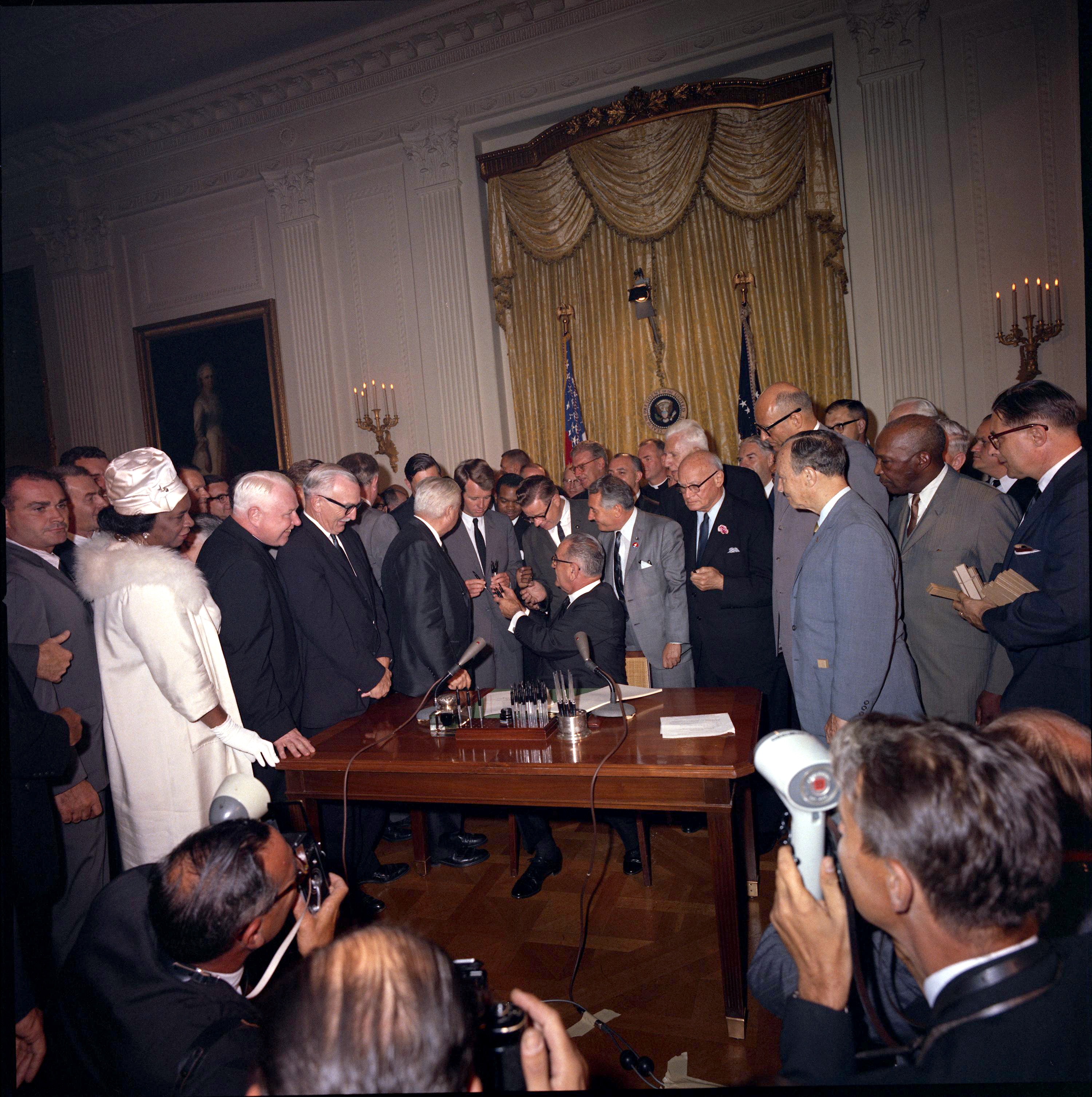 President Lyndon B. Johnson hands bill signing pen to Attorney General Robert F. Kennedy. Others looking on include Dr. Rosa Gragg, Sen. Wayne Morse, Cong. Peter Rodino, Cong. Emanuel Celler, Cong. James Roosevelt and A. Philip Randolph.