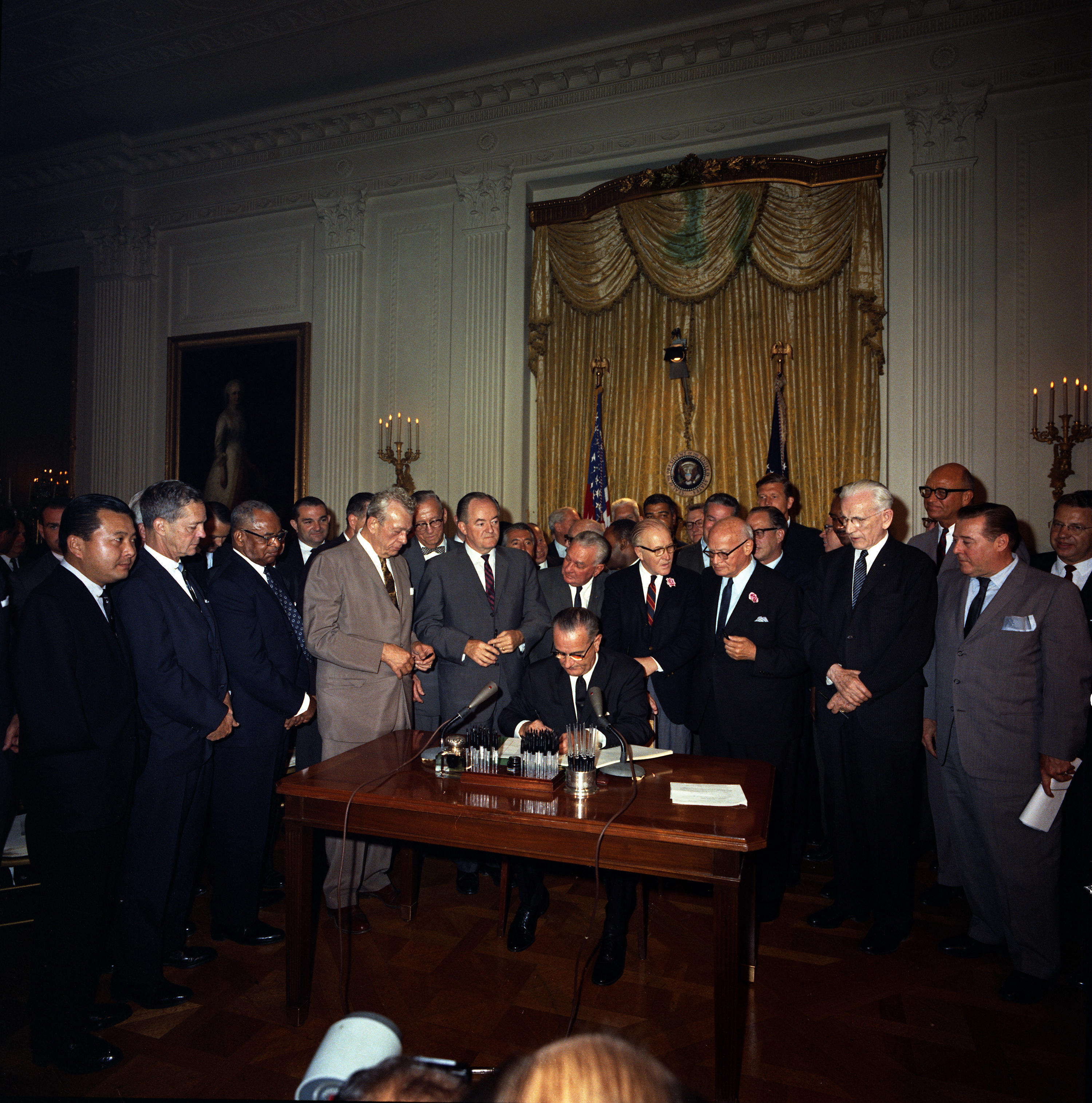 L-R (standing): Sen. Daniel Inouye, Cong. Dan Rostenkowski, Rev. Walter Fauntroy, Sen. Everett Dirksen, Sen. Hubert Humphrey, Cong. Charles Halleck, Cong. William McCulloch, Cong. Emanuel Celler, Speaker John McCormack, Cong. James Roosevelt (behind the Speaker), Sen. Warren Magnuson.