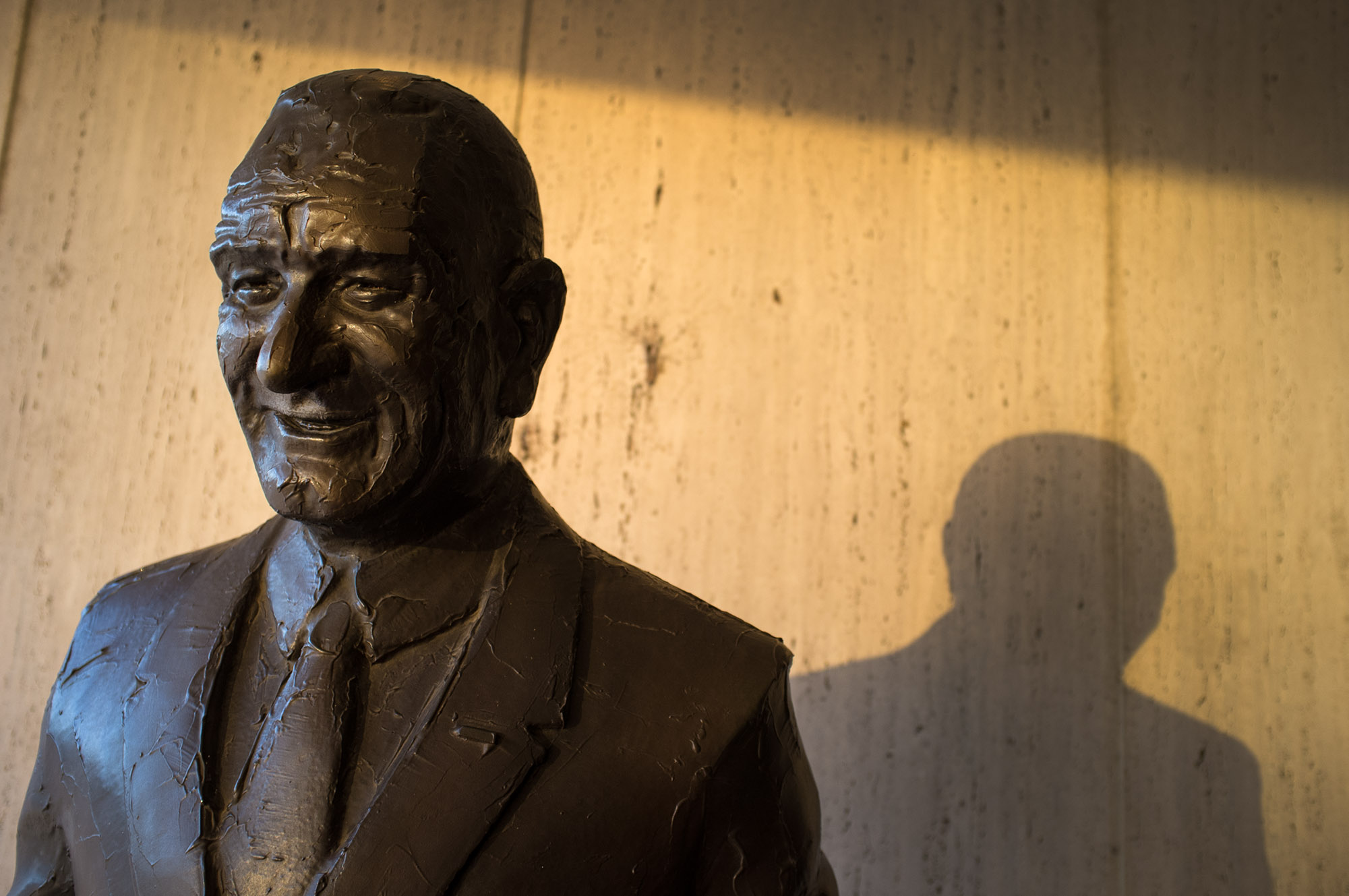 A statue of President Lyndon Baines Johnson in golden light reflected by buildings next to the LBJ Presidential Library.