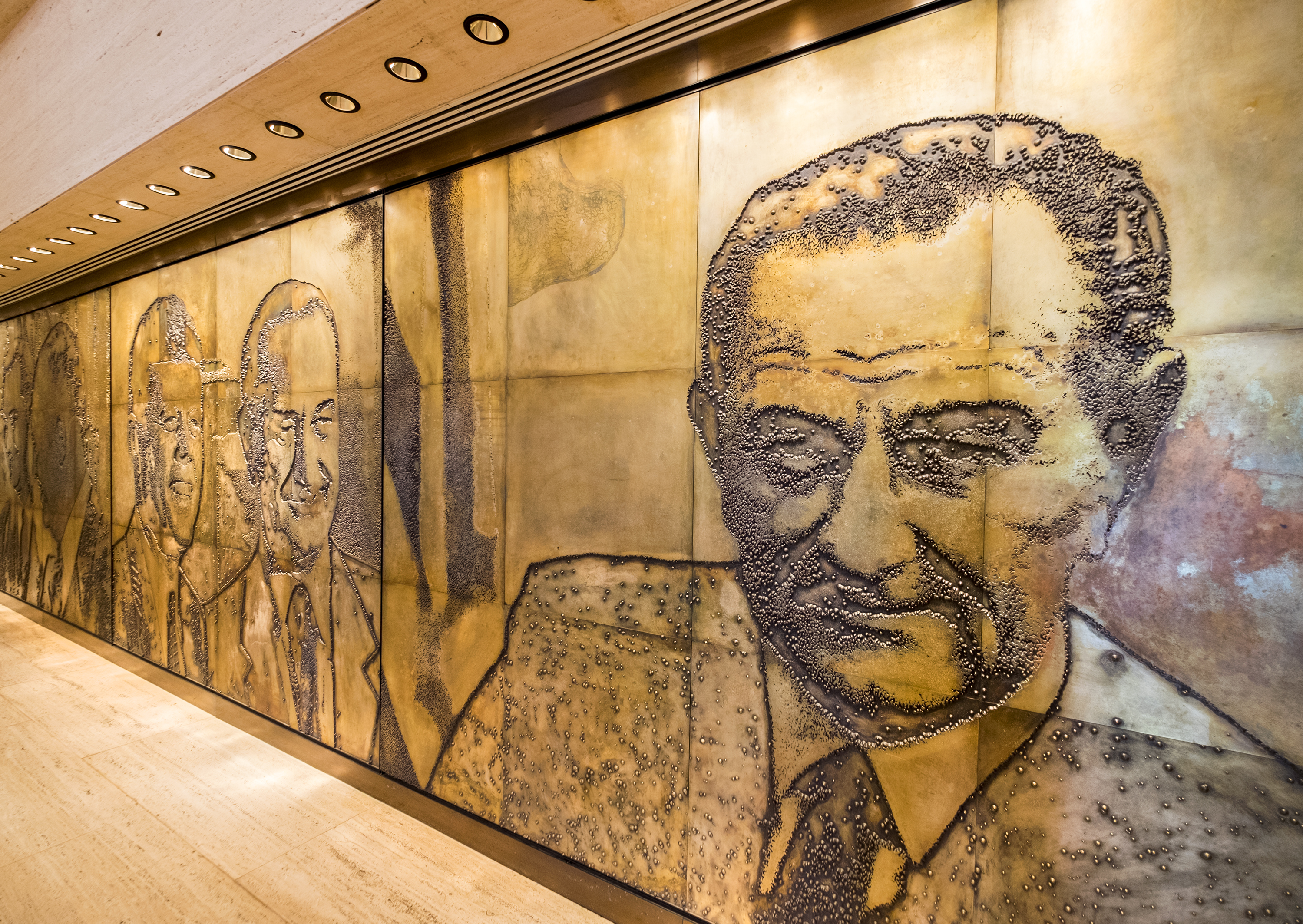 A centerpiece in the Great Hall of the LBJ Library is the photo-engraving mural by artist Naomi Savage. A series of five deeply etched magnesium plates, each 8 feet by 10 feet, portray LBJ as a political figure from the time he arrived in Washington to serve in the House of Representatives in 1937.