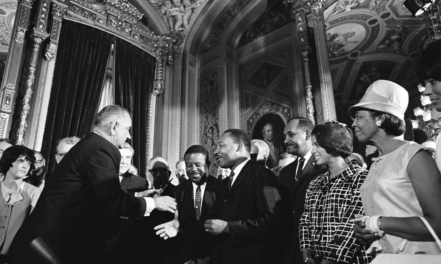 President Lyndon B. Johnson moves to shake hands with Dr. Martin Luther King while others look on, LBJ Library photo by Yoichi Okamoto, A1030-17a