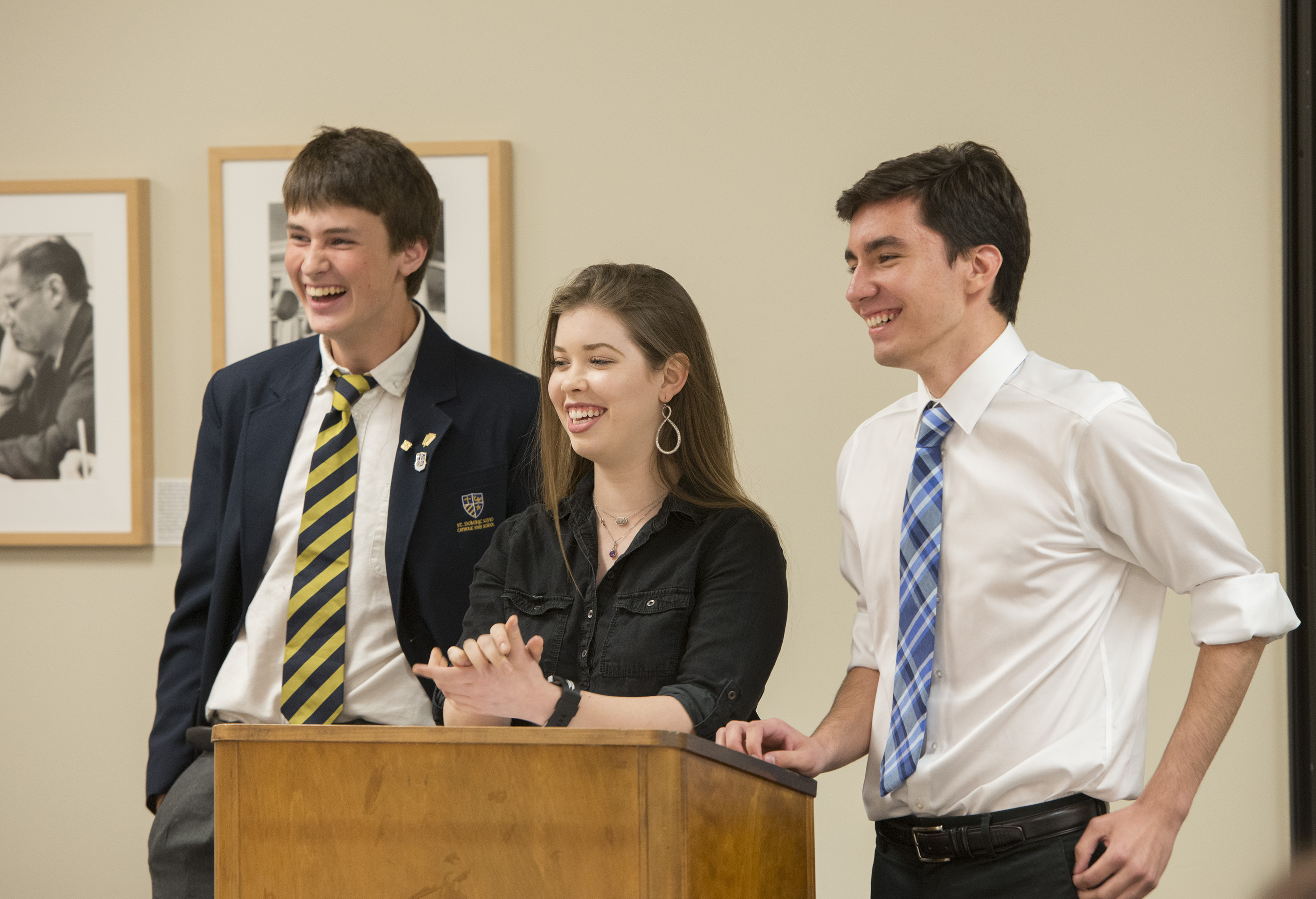 Three students, two male and one female, laugh while standing at the podium presenting their findings during an immersive classroom experience at the LBJ Library.