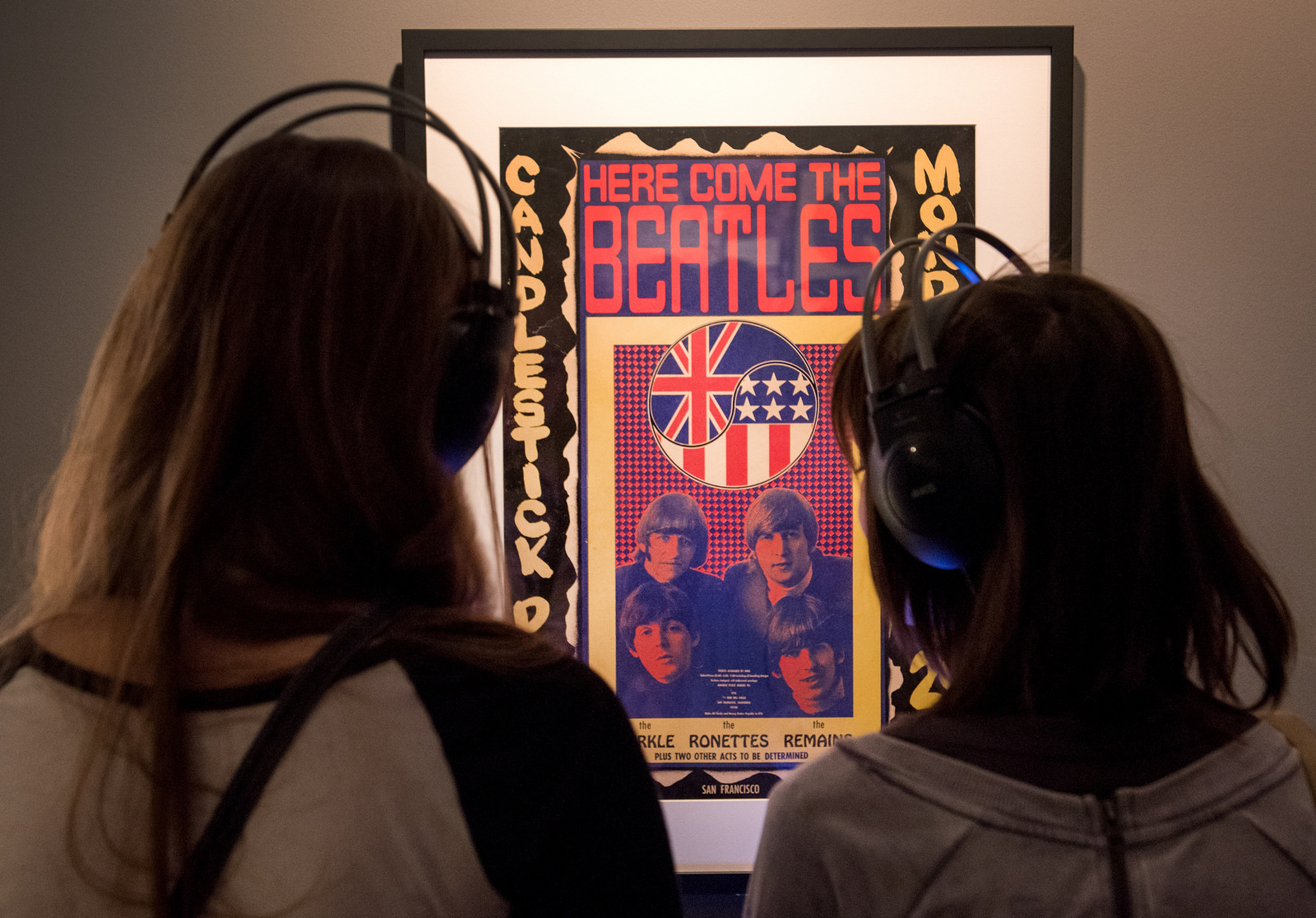 Two visitors, wearing headphones, view a poster in the "Ladies and Gentlemen…The Beatles!" exhibition at the LBJ Library.