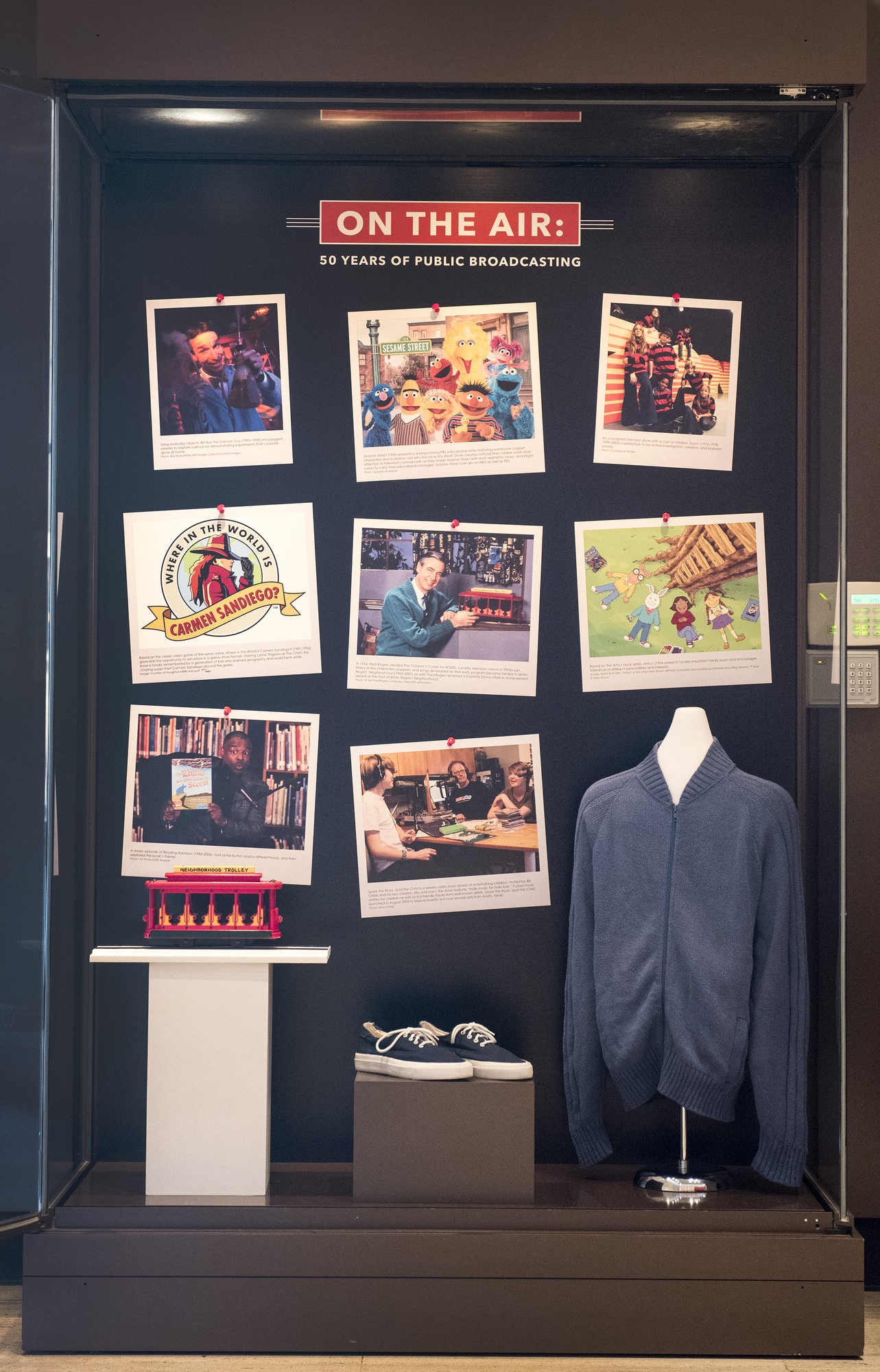 A photo of a glass case displaying several artifacts, including Mr. Rogers' sweater and shoes, that was a part of the "On the Air" exhibition at the LBJ Library.