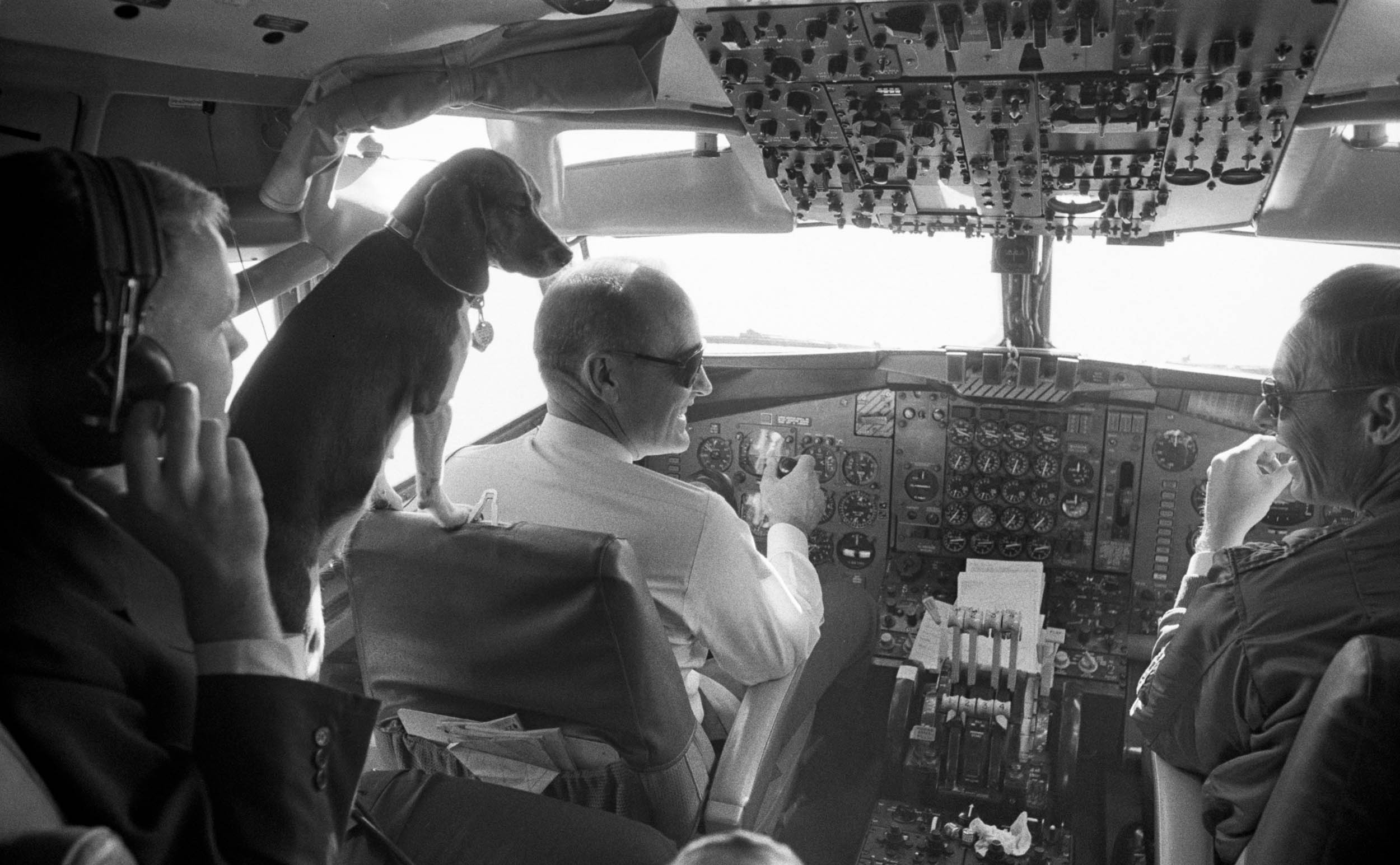 Kim, one of President Lyndon B. Johnson's beagles, looks over the shoulder of Col. James Cross in the Air Force One cockpit.