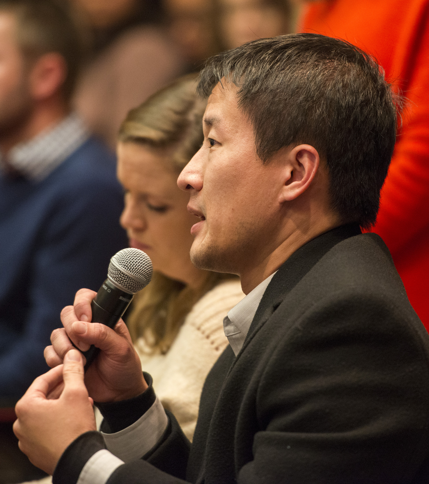 While holding a mic, a member of the audience asks a question during a Future Forum program.