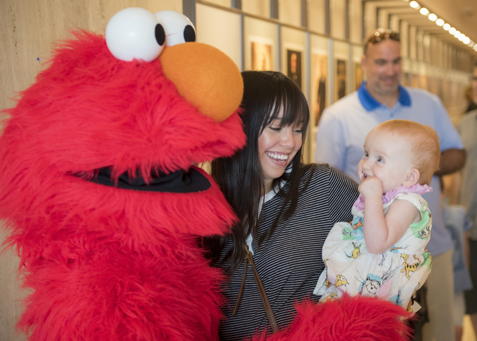 Mother and young child smile while posing with Walkaround Elmo at the opening day of the "On The Air: 50 Years of Public Broadcasting" exhibit at the LBJ Library.