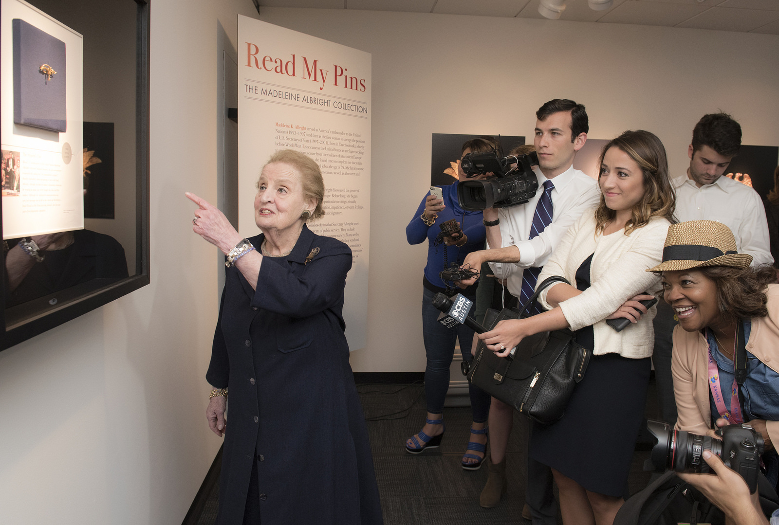 Madeleine Albright points at one of her pins while speaking to the press at the LBJ Library.