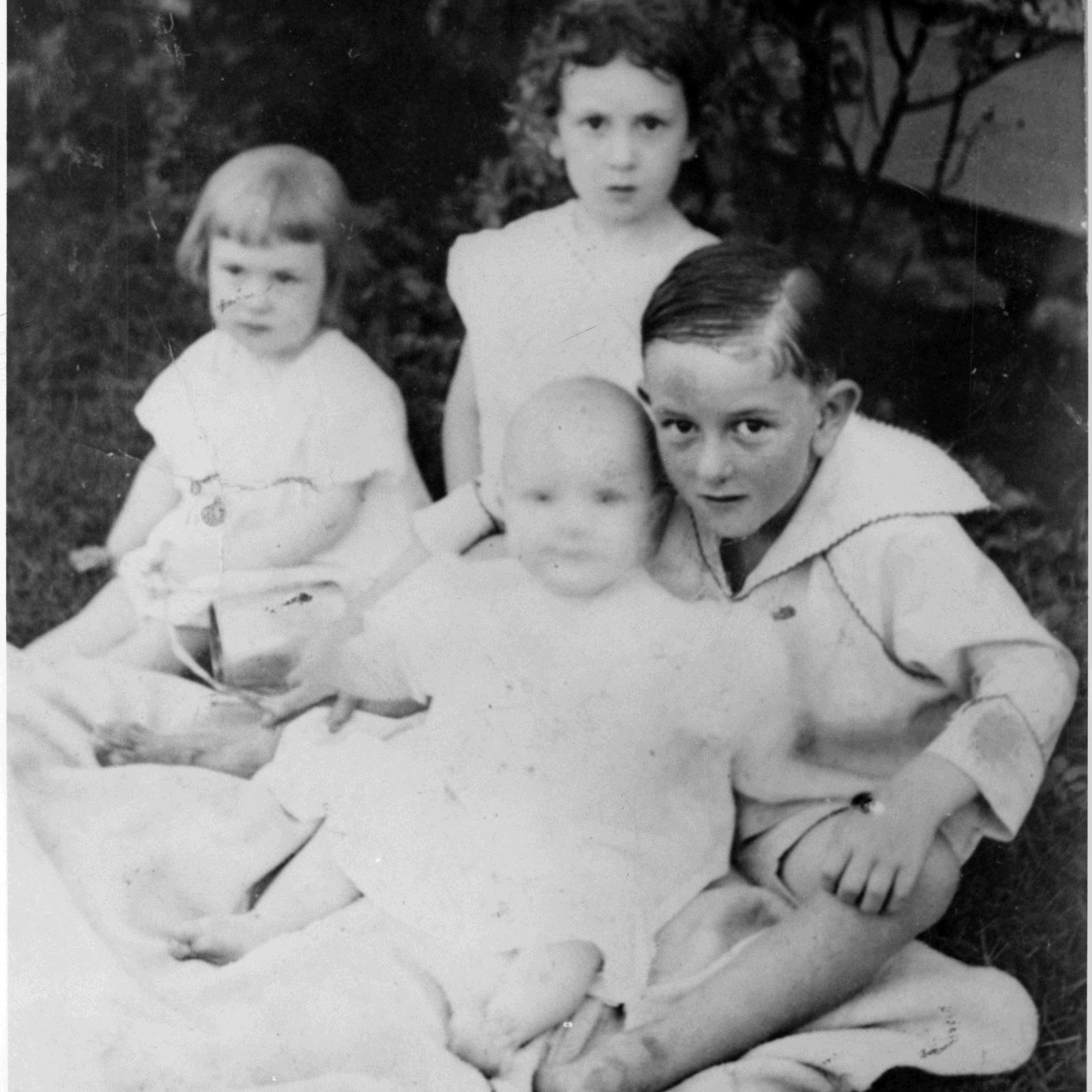 LBJ poses with his three siblings while all seated on a blanket in a yard.