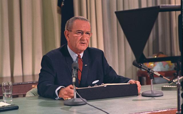 President Lyndon B. Johnson, seated at his desk in the Oval Office, addresses the nation.