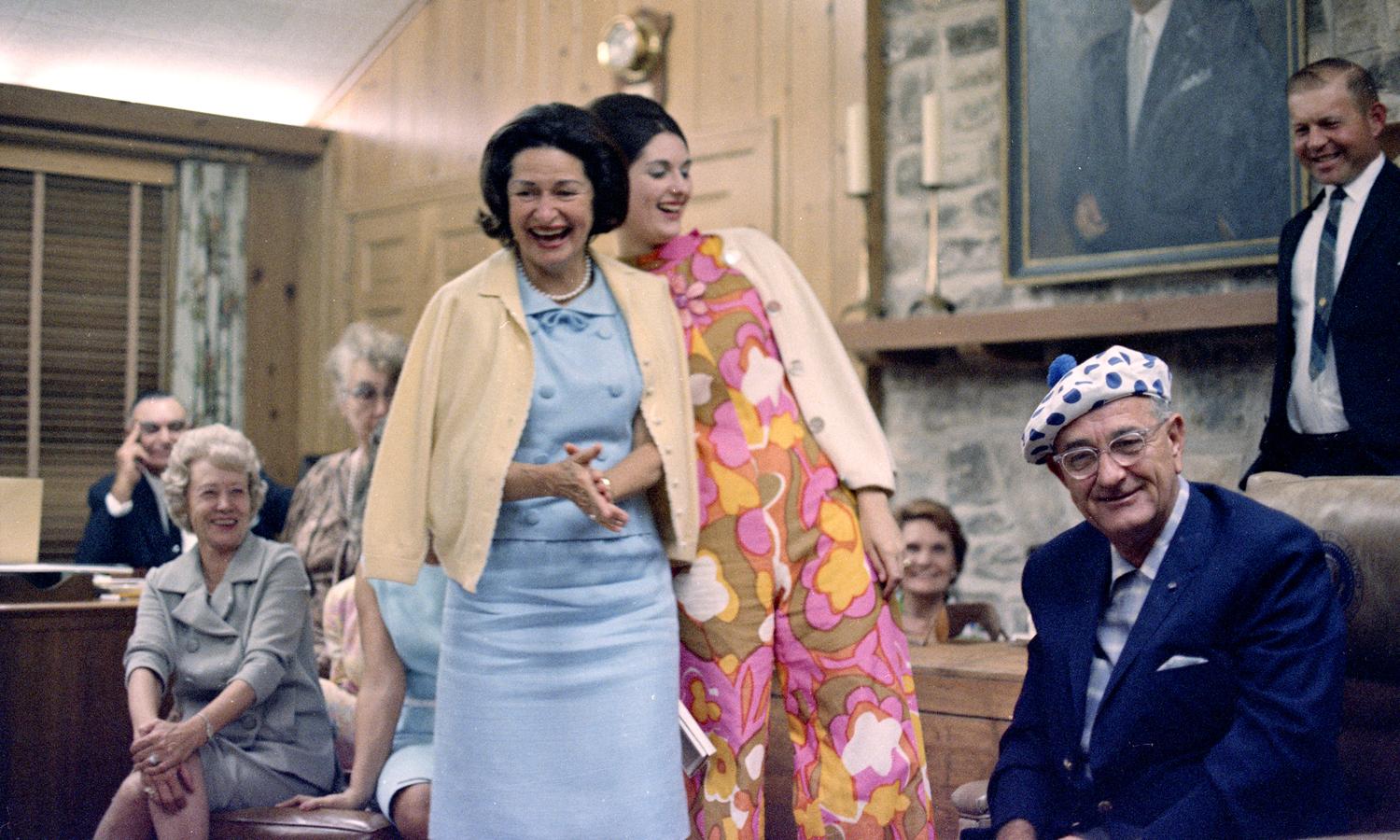 President Johnson wears a blue, polka dotted hat, given to him as a birthday present, as Lady Bird Johnson and daughter Lynda laugh. [LBJ Library photo by Kevin Smith, C2944-16. Aug. 27, 1966.]