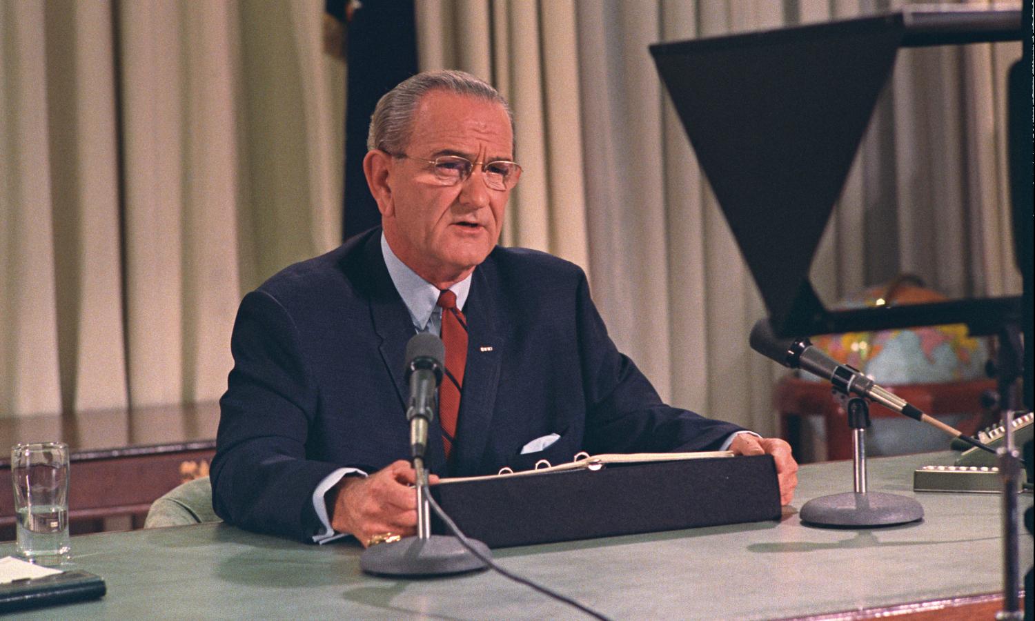 President Lyndon B. Johnson, seated at his desk in the Oval Office, addresses the nation.